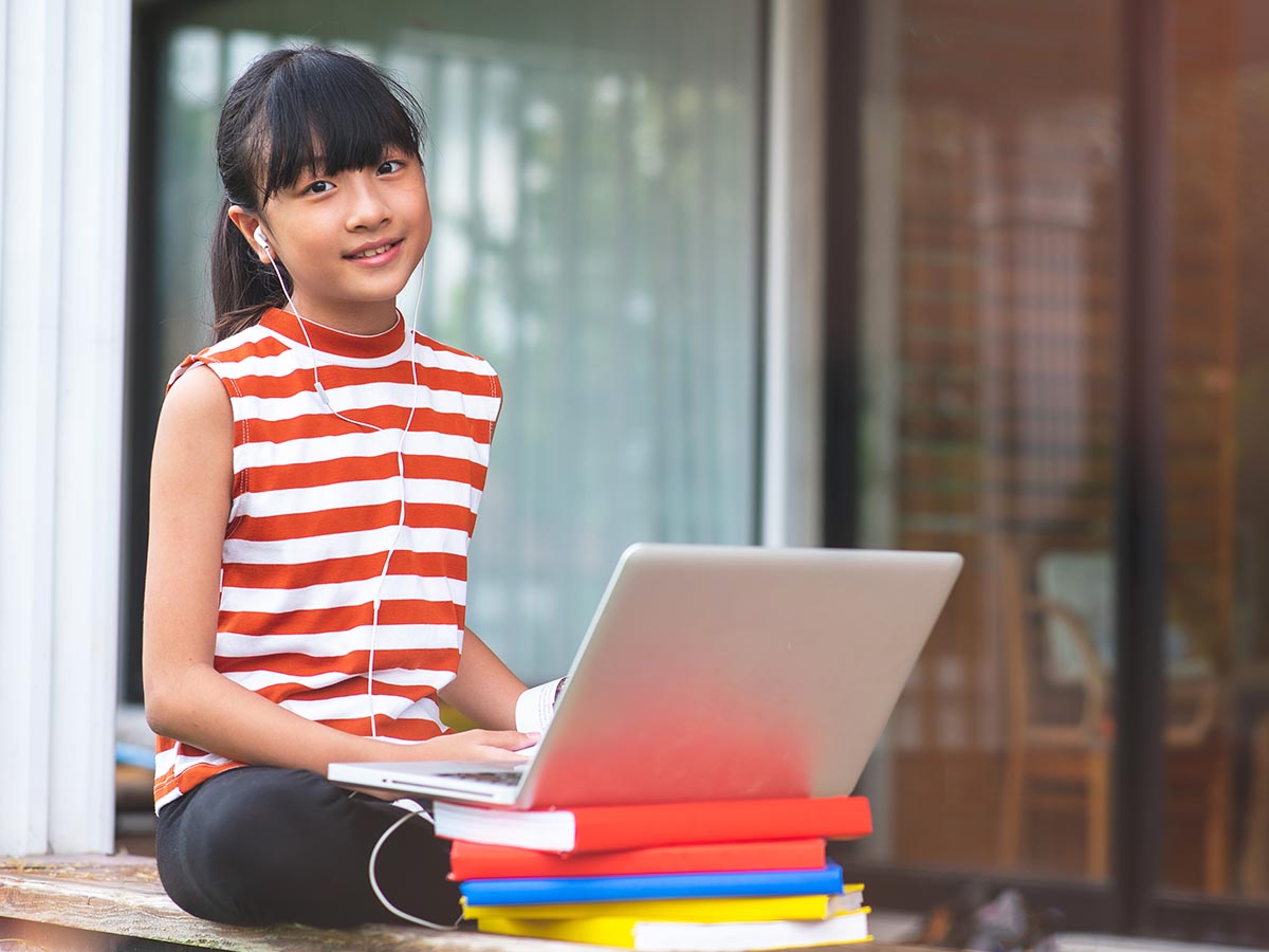 Girl sitting outside using a laptop on a stack of books