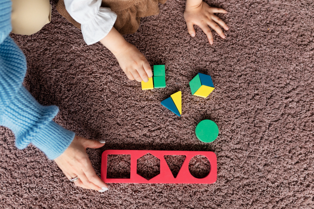 A student practices fitting geometric wooden blocks into a matching tray with a teacher’s guidance.