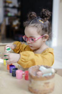 A young girl in a yellow sweater intently focuses on stacking small containers.