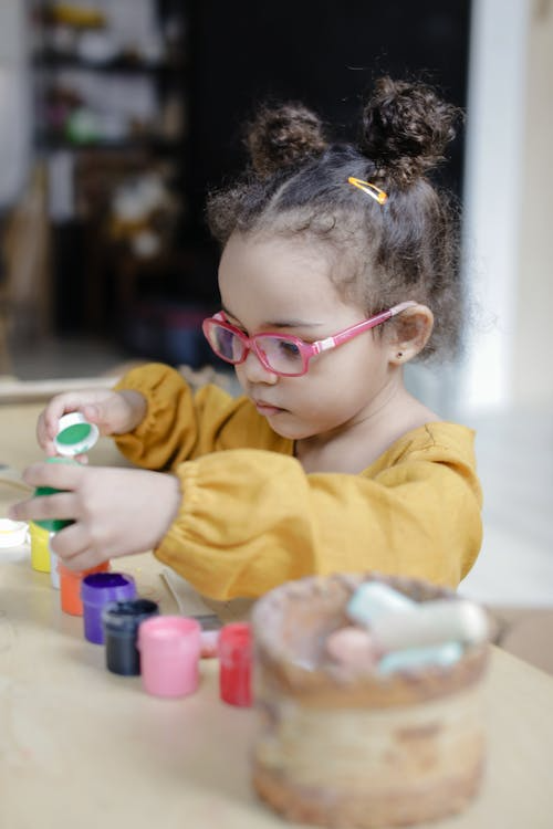 A young girl in a yellow sweater intently focuses on stacking small containers.