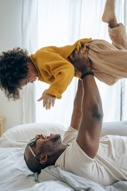 A father playing with his daughter on a bed.