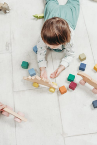 A young child carefully stacks colorful wooden geometric shapes.
