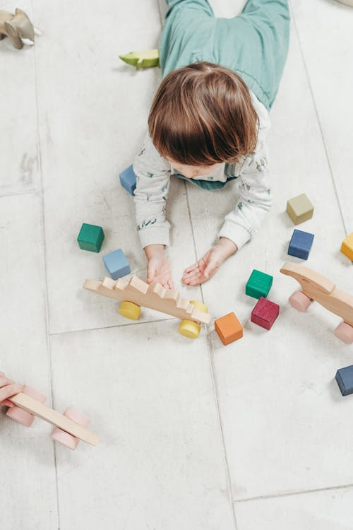 A young child carefully stacks colorful wooden geometric shapes.