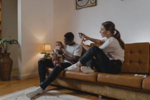 A woman holding a phone photographs a man feeding a toddler at home.
