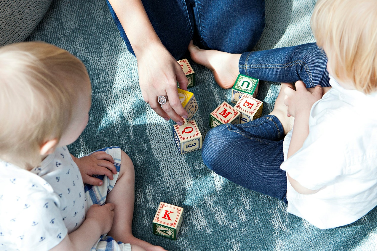 Parent playing letter blocks with two toddlers, encouraging early literacy skills.