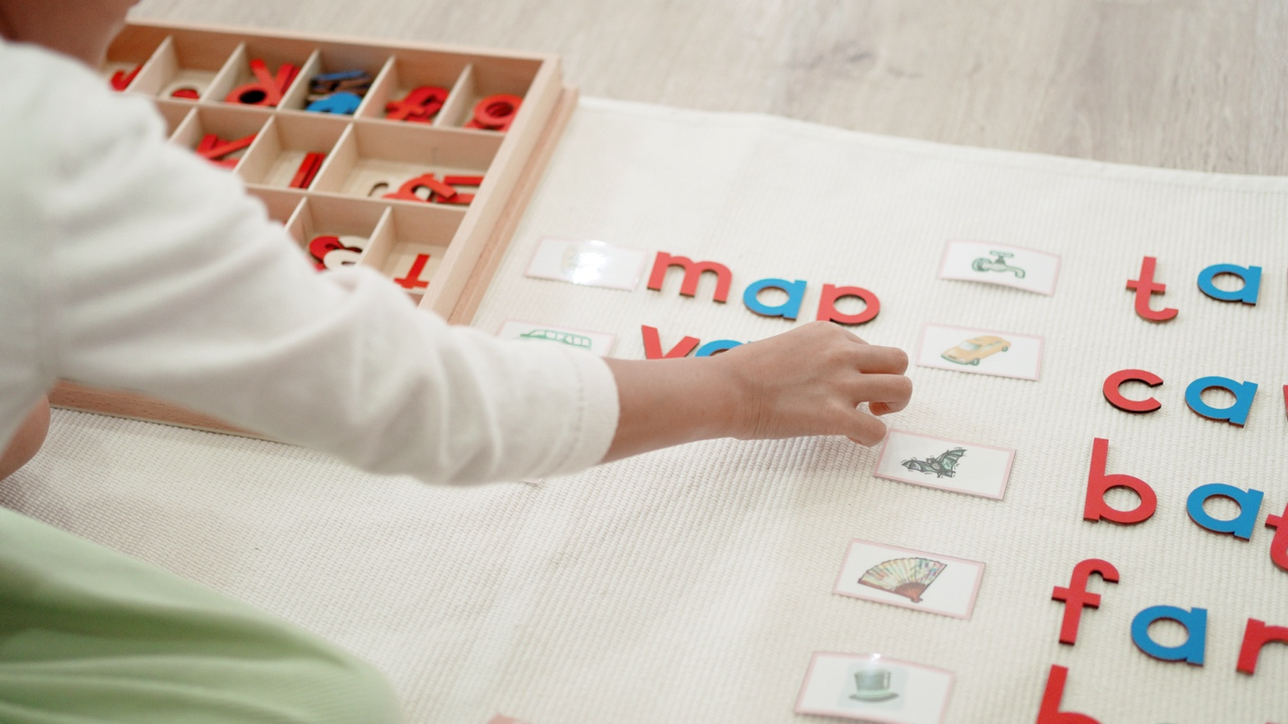 Woman arranging letters beside drawings during a language learning activity.