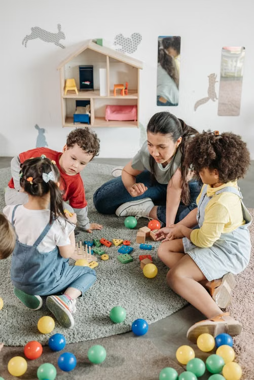 Teacher sitting on the floor with children as they explore balls and other play materials together